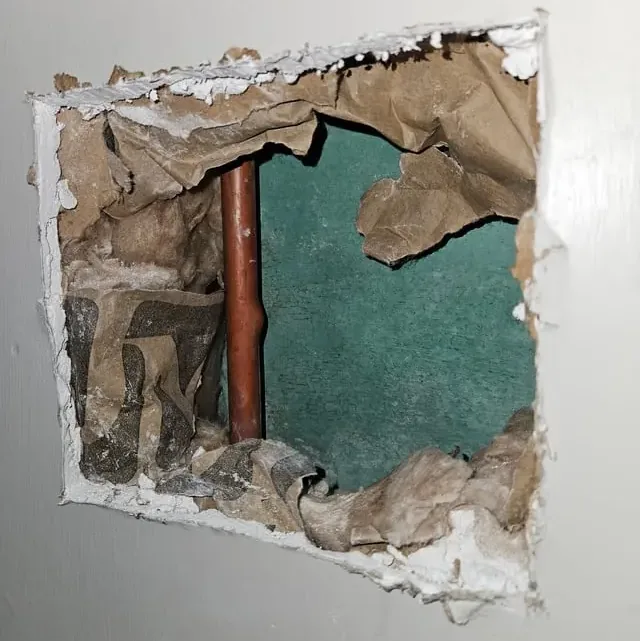 Drywall opened to reach a leaking copper water pipe inside the wall