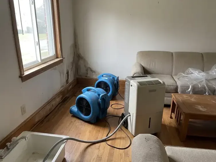 Air movers and a dehumidifier arranged across a living room during water-damage drying