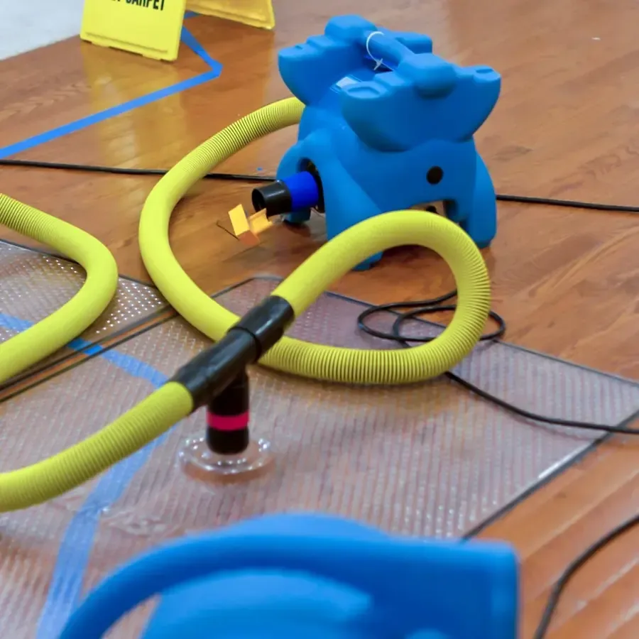 A drying mat and attached hoses cover part of a hardwood floor during moisture removal.