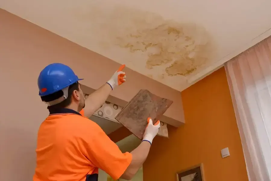 Tech in a hard hat inspecting a roof leak stain on a ceiling