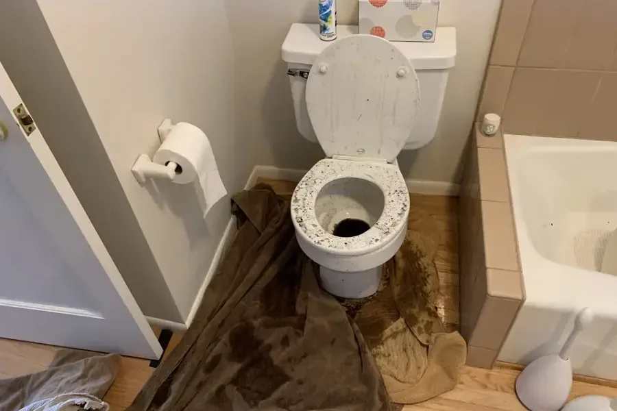Overflowed toilet with soaked towels spread across the bathroom floor